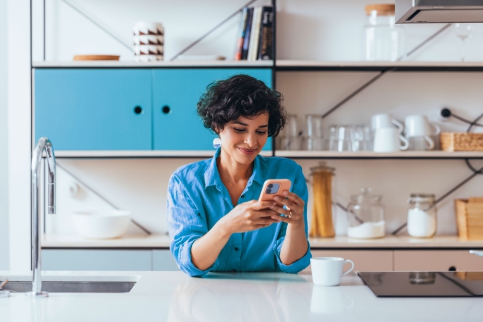 A woman on her mobile phone getting Pay As You Go energy advice using Utilita Energy's Help Centre, while in the kitchen.